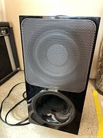 Front view showing grille, bass port and attached cable