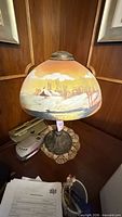 Full view of lamp on table showing painted glass shade and metal base