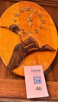 Front view of oval wooden wall clock with carved bird and gold numerals