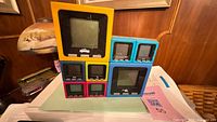 Front view of stacked cube handheld games showing variety of colors and screen damage
