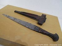 Dagger and scabbard side by side on surface