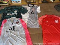 All four soccer shirts laid out: Palmeiras green, Toronto FC grey/white, PSG grey/pink long sleeve, Canada red
