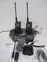 Two radios on charging cradles, third radio with accessories, manual, antennas, cables