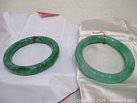 Both jade bangles displayed on fabric pouches