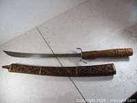 Full view of sword beside carved scabbard