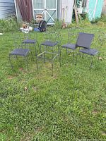 Six wrought iron chairs arranged on grass, some seat pads removed
