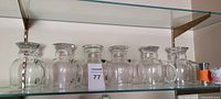 Six clear glass handled beer mugs lined on shelf with shot glass and jigger visible