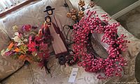 All items arranged on sofa: wreath, figurines, leaf spray, metal stand, brown pod stem
