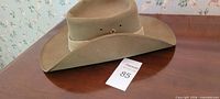 Side view olive green fedora on wooden surface with MaxSold tag