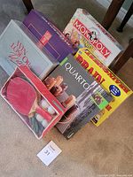 Stack of six games including Monopoly Junior, Balderdash, Win Lose Or Draw, Quarto, Brain Cramp, and ping pong set