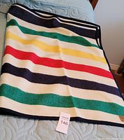 Folded multicolour striped wool blanket on bed showing overall pattern