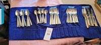 Entire flatware set arranged on blue roll holder showing all utensil groups