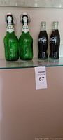 Two green Grolsch bottles and two full Coca-Cola bottles on shelf