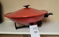 Side view of orange electric wok on stand with lid and power base