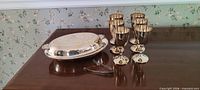 Overall lot showing covered serving dish, six brass goblets, metal tongs