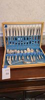 Full view of flatware set in open wood chest showing knives in lid and other pieces in base