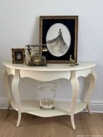 Front view of cream half-moon console table with decorative items on top