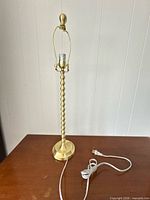 Full view of gold-tone lamp base, harp, finial and cord on table