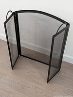 Three-panel black metal mesh fireplace screen standing upright