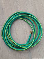 Coiled green garden hose with yellow stripes and brass end fitting visible