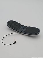 Speaker open showing dual black grilles and hinged design with attached 3.5 mm plug cable