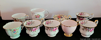 Front view of all eight teacups and one saucer displaying patterns and colours