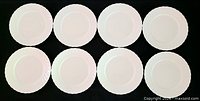 Eight white scalloped-rim bone china plates displayed