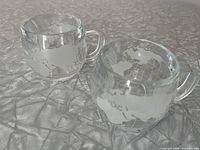 Pair of clear glass globe mugs side by side showing etched world map pattern