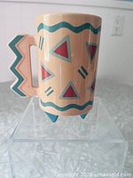 Front view of ceramic mug showing geometric pattern, handle and tripod feet