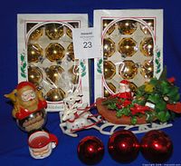 Front view showing two boxes of 12 gold ornaments, Santa snow globe, plastic sleigh with Santa, three red ornaments and mini Santa mug candle