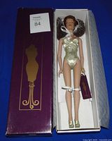 Doll in open box next to purple lid, full body view with accessories visible