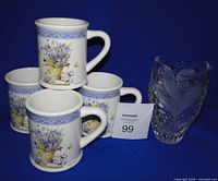 Four floral mugs stacked with crystal vase beside