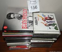 Two stacks of CDs on wooden surface showing covers Elvis Presley and ABBA