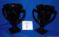Front view of both black amethyst glass trophy vases showing handles and embossed nymphs