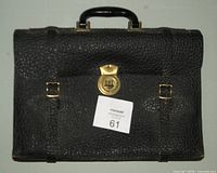 Front view of black leather satchel showing brass clasp, buckles and handle