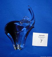 Full view of clear art glass elephant figurine with trunk up against blue backdrop