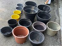 All 15 plastic pots grouped on pavement, showing varying sizes and colours
