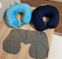 All three neck pillows laid out: blue fabric, light blue plush, grey inflatable (deflated)