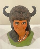 Front view of ceramic bust showing facial detail, buffalo headdress, necklace, and green base