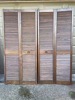 Two brown louvered bi-fold doors standing upright