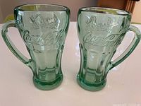 Front view of both green Coca-Cola mugs