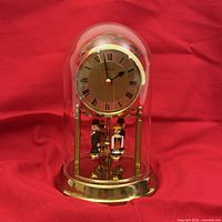 Front view of clock with glass dome in place showing dial, dancers and brass base