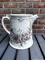 Side view of white pitcher with floral design, handle and spout visible