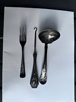 Fork, shoe button hook, and ladle laid out on white background
