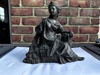 Front view of cast metal seated female figure on base