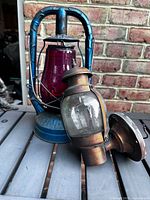 Blue Dietz Monarch lantern with red globe beside copper/brass wall sconce