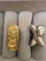 Both rings in display slot; shows elongated Egyptian motif ring and two-tone ring side by side