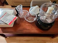 All components laid out on table including storage case, bowls, lid, juicer attachment and manual