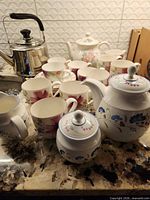 Group shot showing both teapots, stainless kettle, sugar bowl, creamer and multiple teacups