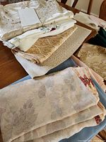 Stacked assorted patterned tablecloths and runners in ivory, gold, blue, floral